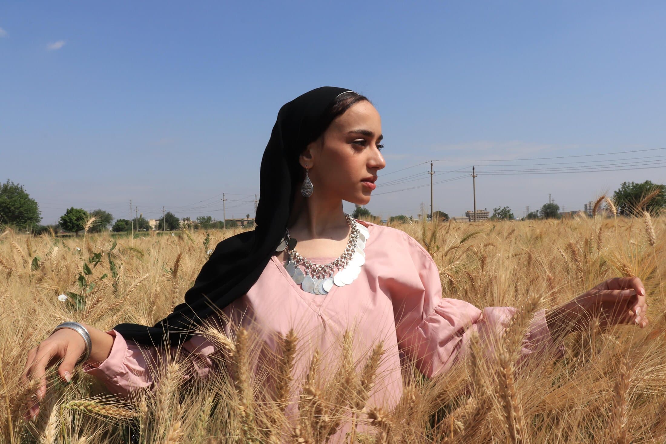 A woman in a wheat field wearing a Hilya silver coin necklace, earrings, and bangle